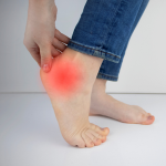 Topuk Dikeni hastalığına sahip bir kadın, ağrıyan topuğunu tutarken. Bu fotoğrafta, Topuk Dikeni nedeniyle topuğu ağrıyan bir kadının portresi. Topuk Dikeni hastalığından kaynaklanan topuk ağrısını yaşayan bir kadının görüntüsü.